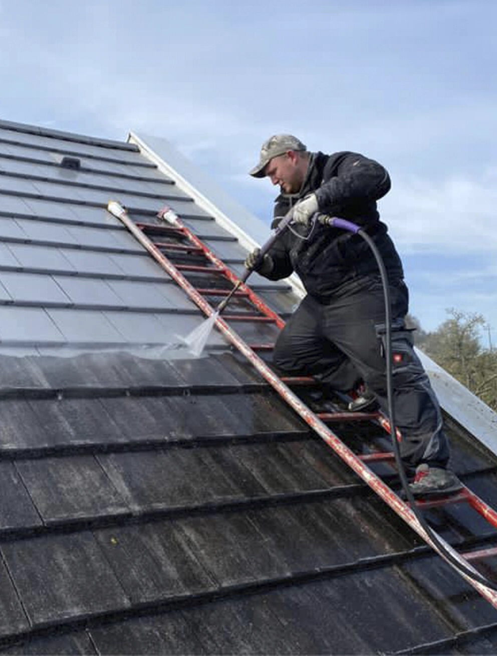 Facharbeiter reinigt ein Ziegeldach materialschonend mit druckreduzierter Technik zur Entfernung von Moos und Algen.