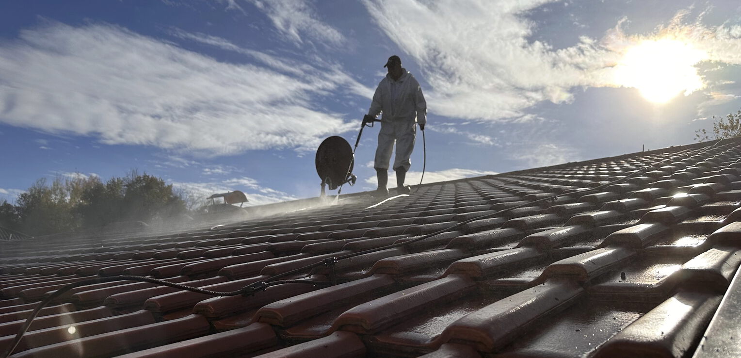 Professionelle Dachreinigung: Facharbeiter entfernt Verschmutzungen von Dachziegeln mit Spezialgerät bei sonnigem Wetter.