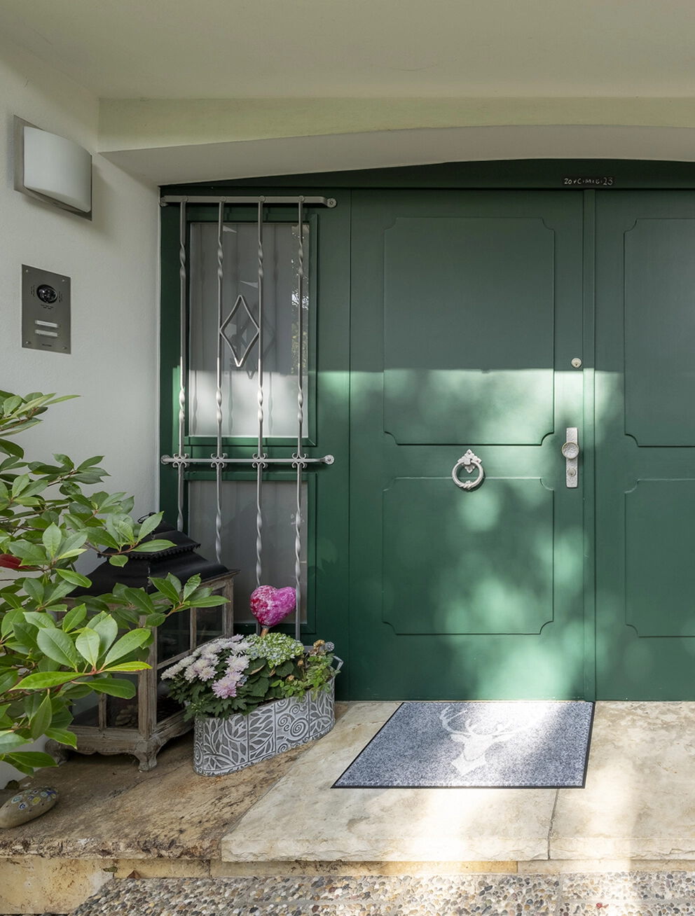 Eingangsbereich eines Wohnhauses mit grün gestrichener Haustür, dekorativen Pflanzen und gepflegter Naturstein-Treppe vor der Fassade.
